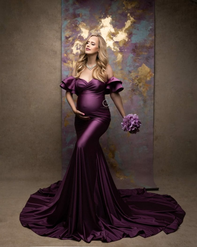 Expectant mom in a chic plum dress stands before an artfully designed droplet backdrop.